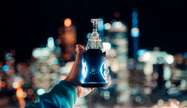 Someone is holding an electric dab rig in front of a city skyline.